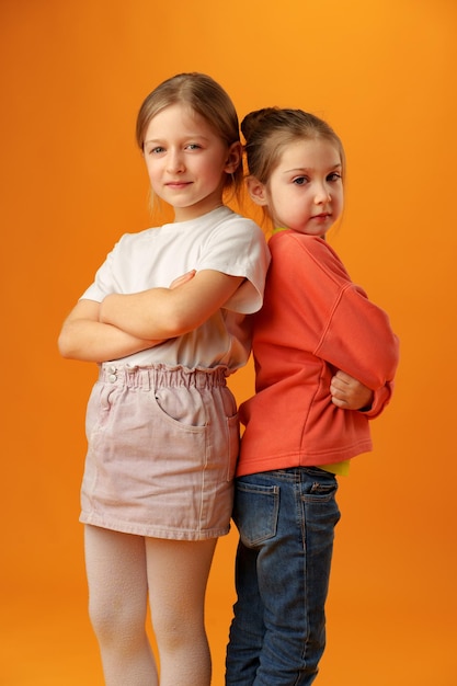 Twee schattige kleine meisjes staan op gele achtergrond in de studio