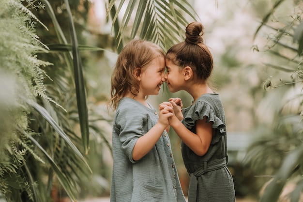 Twee schattige lachende kleine meisjes in linnen kleding hand in hand en wandelen in de botanische tuin