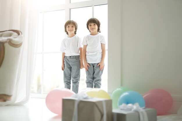 Twee schattige latijnse tweelingjongens, kleine kinderen in vrijetijdskleding die er gelukkig uitzien, hun ouders begroeten, kleurrijke ballonnen en geschenkdozen voor hen voorbereiden. Vakantie, cadeautjes, kinderconcept