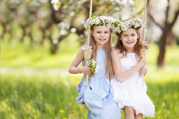 Twee schattige meisjes die plezier hebben op een schommel in de bloeiende oude appelboomtuin. Zonnige dag. Lente buitenactiviteiten voor kinderen
