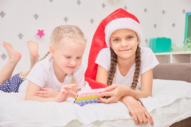 Twee schattige meisjes liggen op het bed en spelen smartphonegames, kerstvakantieconcept, videogesprek met familieleden