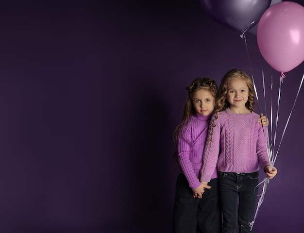 Twee schattige meisjes met ballonnen knuffelen op een paarse achtergrond, een plek voor tekst