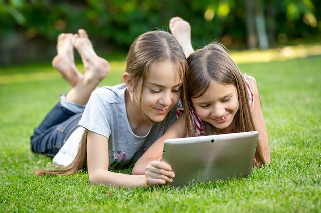 Twee schattige meisjes ontspannen op het gras in het park en het gebruik van digitale tablet