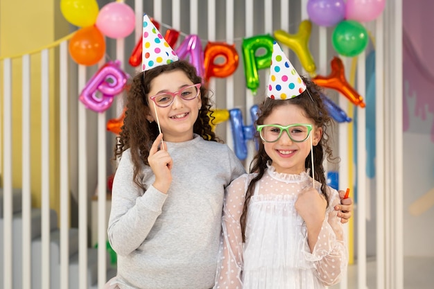 Twee schattige meisjes poseren tegen een fleurige muur met ballonnen op een kinderfeestje