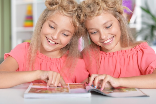 Twee schattige tweelingzussen met moderne kapsels die tijdschrift lezen