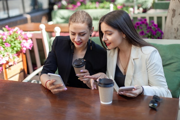 Twee schattige vriendinnen kijken naar een smartphone op het scherm terwijl ze aan tafel zitten op een terras