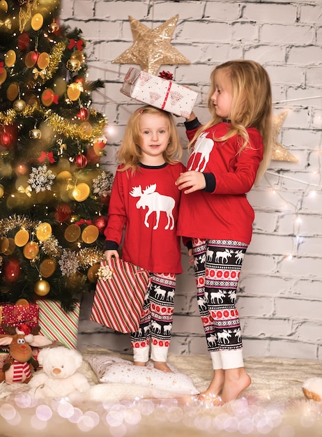 Twee schattige vrolijke meisjes in kerstkleding tegen de achtergrond van de kerstboom