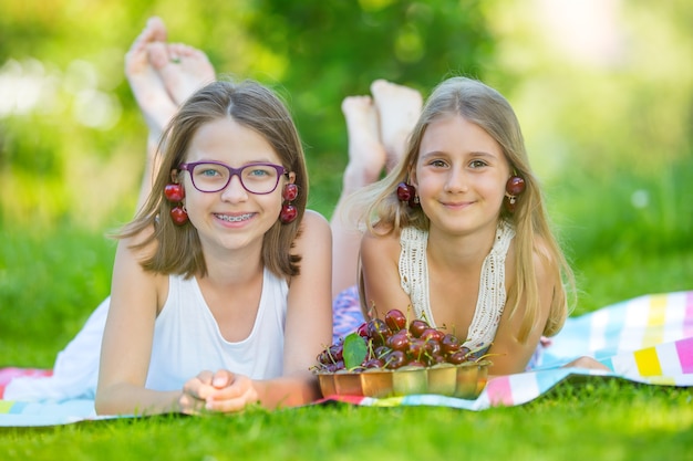 Twee schattige zussen of vrienden in een picknicktuin liggen op een terras en eten vers geplukte kersen.