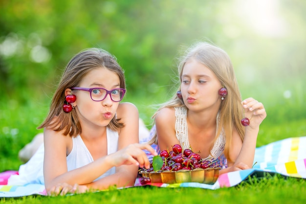 Twee schattige zussen of vrienden in een picknicktuin liggen op een terras en eten vers geplukte kersen.