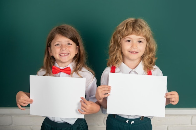 Twee schoolkinderen die een witte papieren blanco poster met kopieerruimte vriendelijke klasgenoten op schoolunifor houden