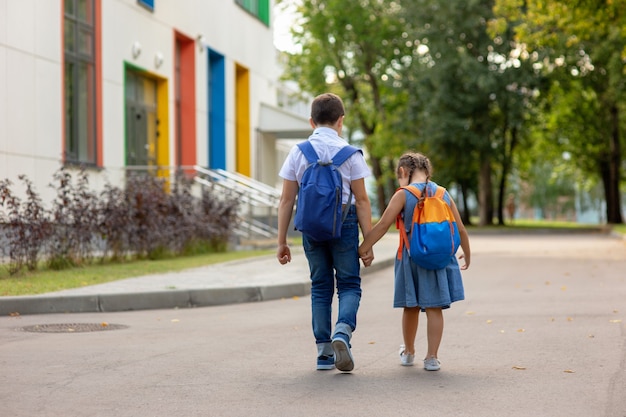 Twee schoolkinderen, een klein meisje en een jongen in een rugzak met rugzakken gaan op weg naar school