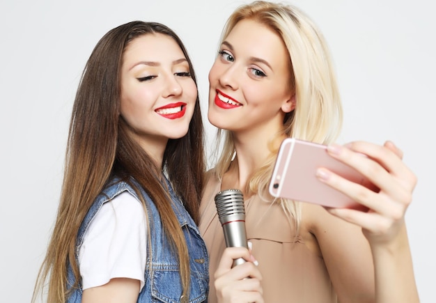 Twee schoonheidsmeisjes met een microfoon nemen selfie met smartphone