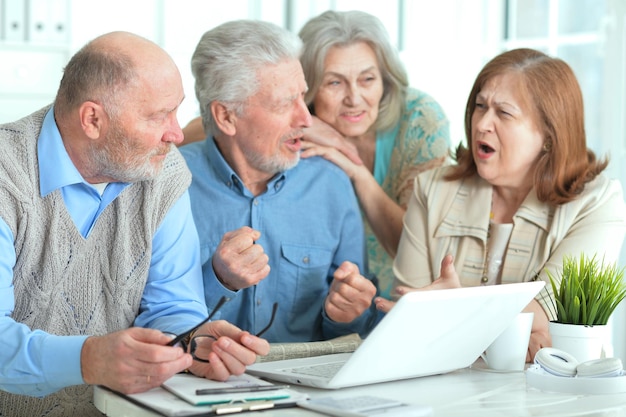 Twee senior koppels zitten aan tafel en werken met laptop