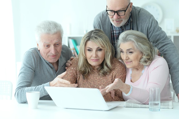 Twee senior paren zitten aan tafel en kijken naar laptop