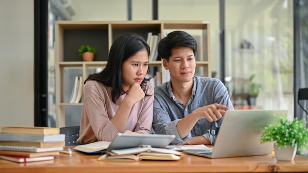 Twee serieuze en gefocuste Aziatische studenten kijken naar een laptopscherm en bespreken werk