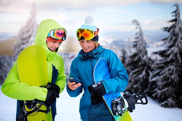 Twee snowboarders praten en houden smartphones vast vrienden kijken naar mobiele telefoon en communiceren in sociaal netwerk en delen hun foto's in app met internetverbinding die kleurrijke mode-outfit dragen