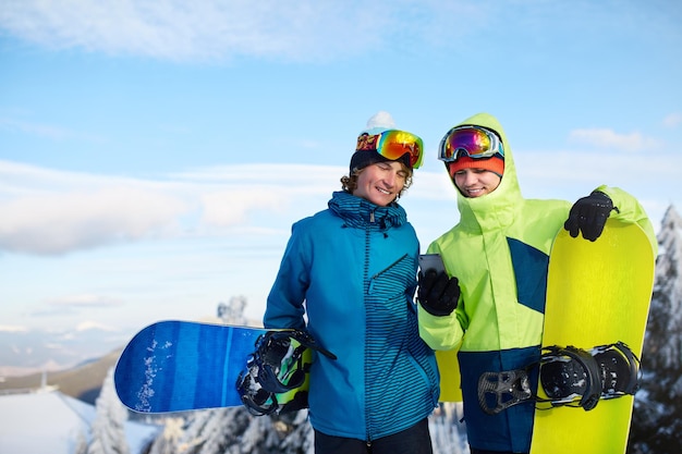 Twee snowboarders praten en houden smartphones vast Vrienden kijken naar mobiele telefoon en communiceren in sociaal netwerk en delen hun foto's in app met internetverbinding die kleurrijke mode-outfit dragen