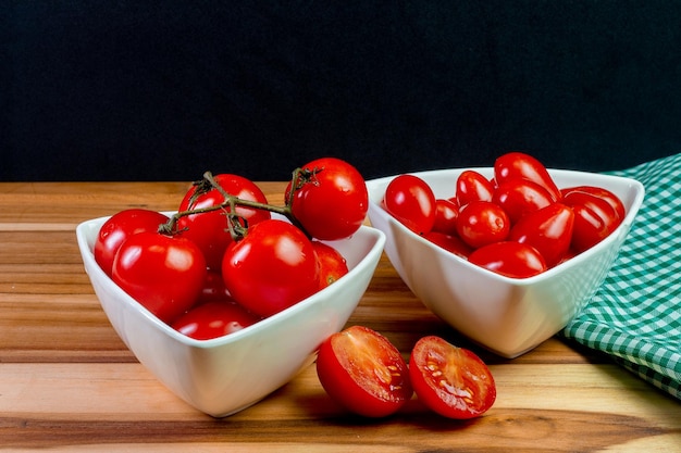 Twee soorten tomaat in een witte kom op een houten tafel met een zwarte achtergrond