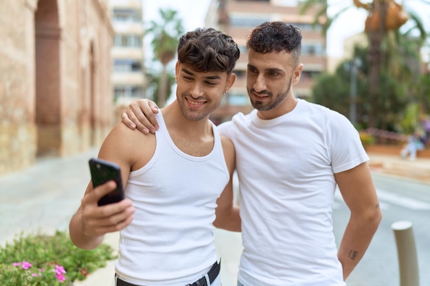 Twee Spaanse mannen paar glimlachend zelfverzekerd met behulp van smartphone op straat