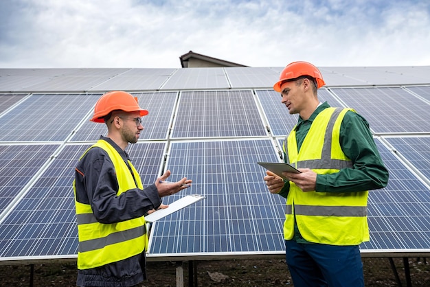 Twee sterke bekwame mannen in helmen en vesten staan en praten in zonnepanelen Groen elektriciteitsconcept