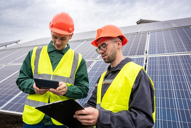 Twee sterke bekwame mannen in helmen en vesten staan te praten in zonnepanelen. Groene stroom concept