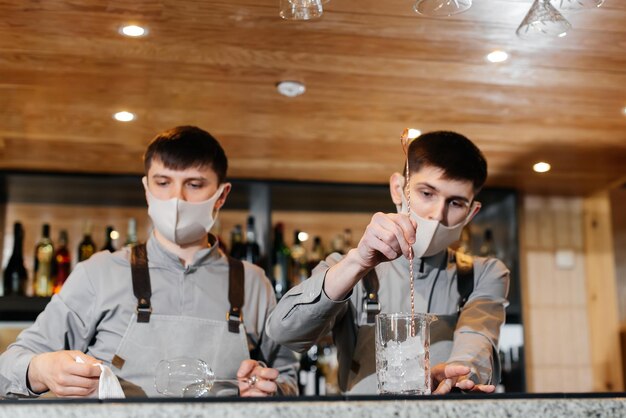 Twee stijlvolle barmannen in maskers en uniformen bereiden cocktails op een feestje tijdens een pandemie het werk van restaurants en cafés tijdens de pandemie