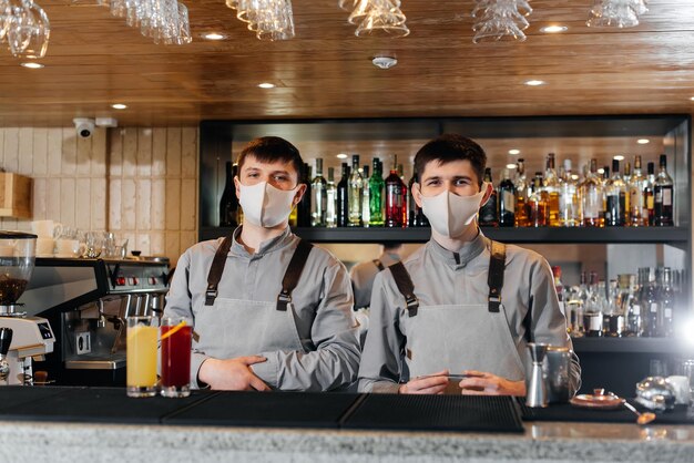 Twee stijlvolle barmannen in maskers en uniformen bereiden cocktails op een feestje tijdens een pandemie Het werk van restaurants en cafés tijdens de pandemie