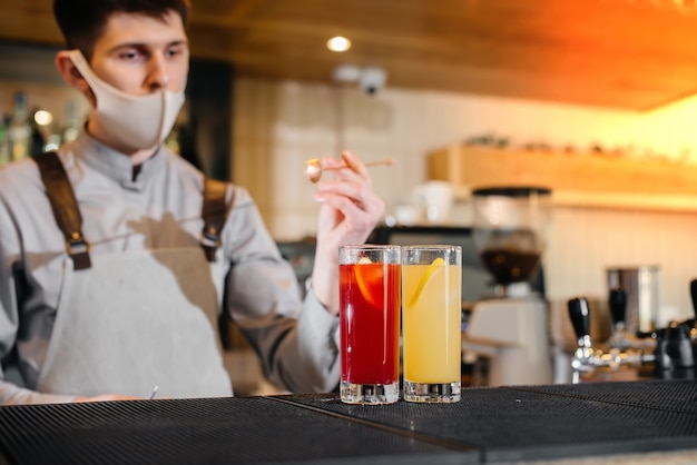 Twee stijlvolle barmannen in maskers en uniformen tijdens de pandemie, cocktails bereiden. het werk van restaurants en cafés tijdens de pandemie.