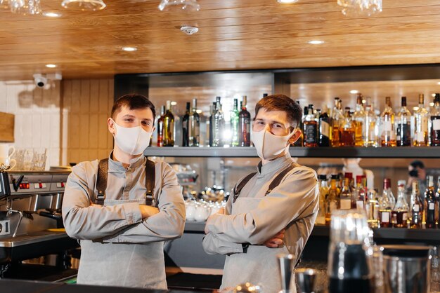 Twee stijlvolle barmannen in maskers en uniformen tijdens de pandemie staan achter de bar het werk van restaurants en cafés tijdens de pandemie