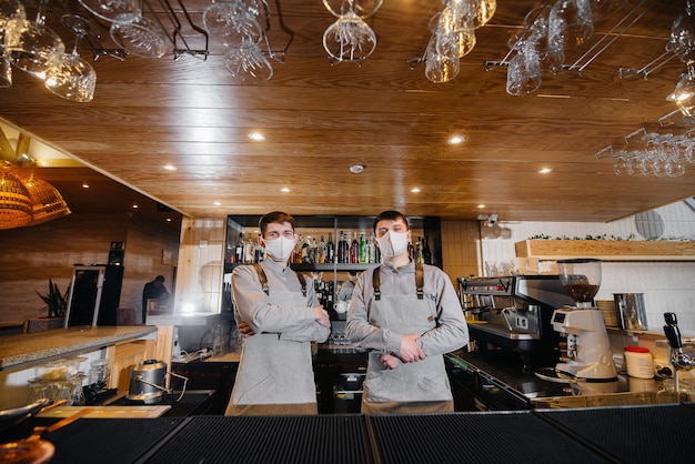 Twee stijlvolle barmannen in maskers en uniformen tijdens de pandemie, staan achter de bar