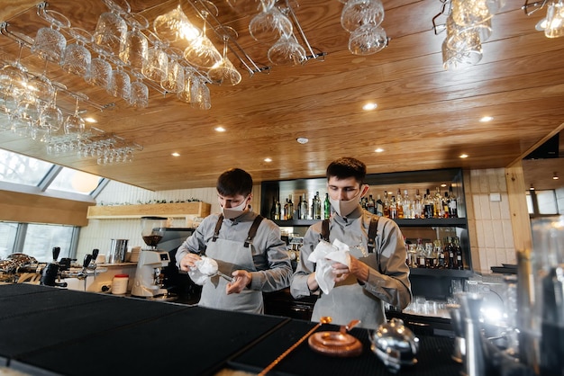 Twee stijlvolle barmannen in maskers en uniformen tijdens de pandemie wrijven een bril om te glanzen het werk van restaurants en cafés tijdens de pandemie