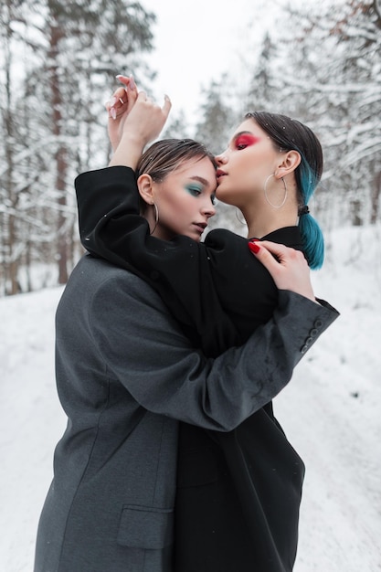 Twee stijlvolle mooie vrouwen met kleurrijke make-up in modieuze kleding met een vintage blazer poseert buiten met sneeuw. Verliefd stel