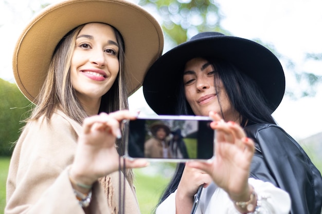 Twee stijlvolle vrienden pakken allebei een mobiele telefoon om een selfie te maken