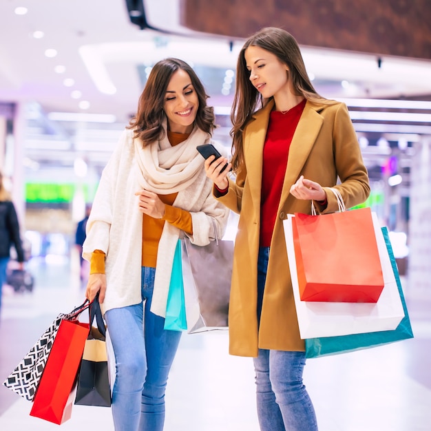 Twee stijlvolle zelfverzekerde vrouwen tijdens het winkelen in het winkelcentrum