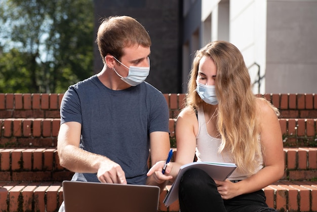 Twee studenten met maskers die naar een laptop wijzen terwijl ze op de trap zitten