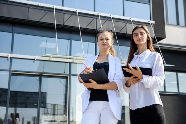 Twee succesvolle en jonge zakenvrouwen met tablet in de buurt van kantoorgebouw