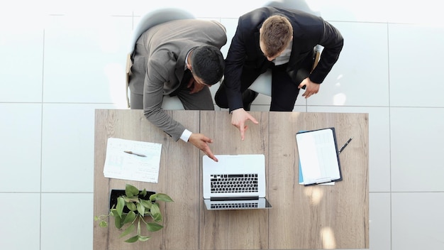 Twee succesvolle lachende zakenlieden werken van bovenaf aan een laptopweergave