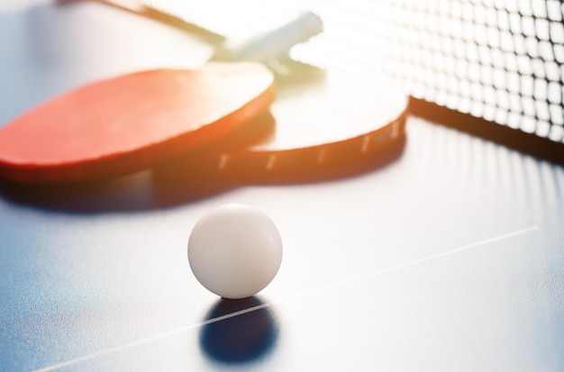 Twee tennisrackets en een witte bal liggen op een tennistafel in de buurt van het net Actieve recreatie en pingpong spelen