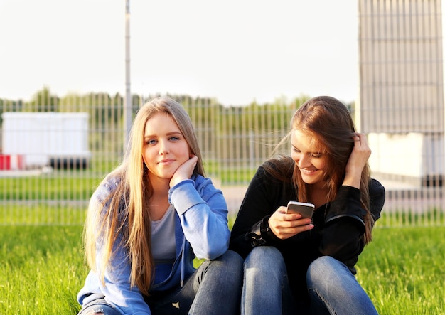 Twee tienermeisjes die een smartphone gebruiken en een selfie maken terwijl ze bij elkaar zitten Twee lachende en grimassen trekkende meisjes
