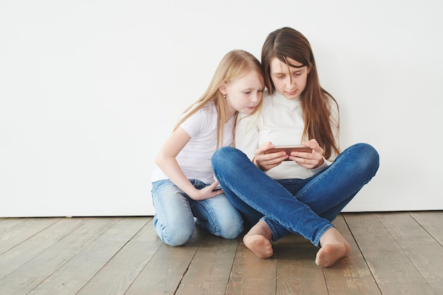 Twee tienermeisjes op een witte achtergrond die spelletjes spelen op de telefoon. gokverslaving
