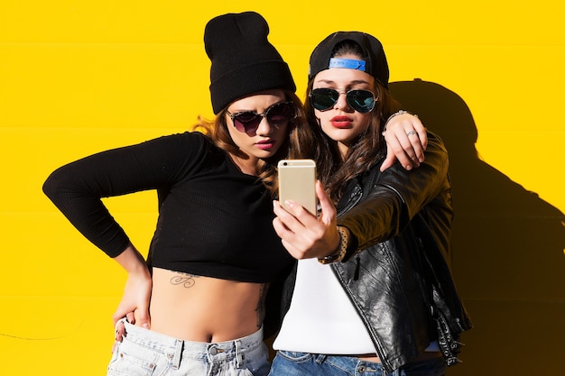 Twee tienermeisjes vrienden in hipster outfit buiten maken selfie op een telefoon