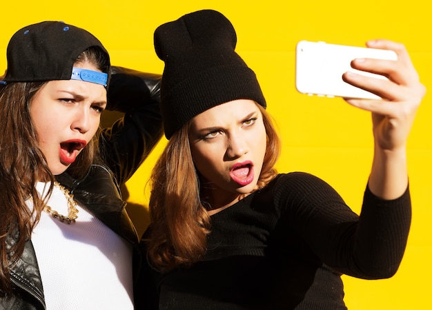 Twee tienermeisjes vrienden in hipster outfit buiten maken selfie op een telefoon.