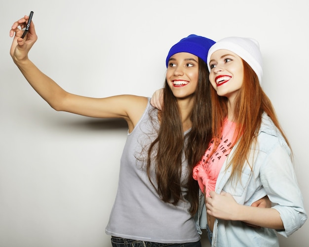 Twee tienermeisjes vrienden in hipster outfit maken selfie op een telefoon.