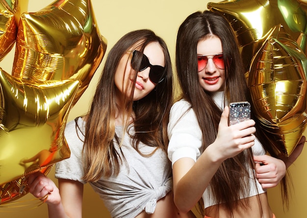 Twee tienermeisjes vrienden met gouden ballonnen maken selfie op ap