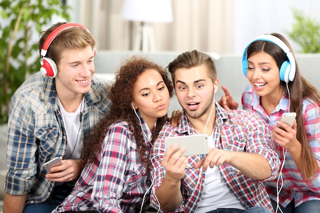 Twee tienerparen luisteren naar muziek en nemen foto met mobiele telefoon in de woonkamer