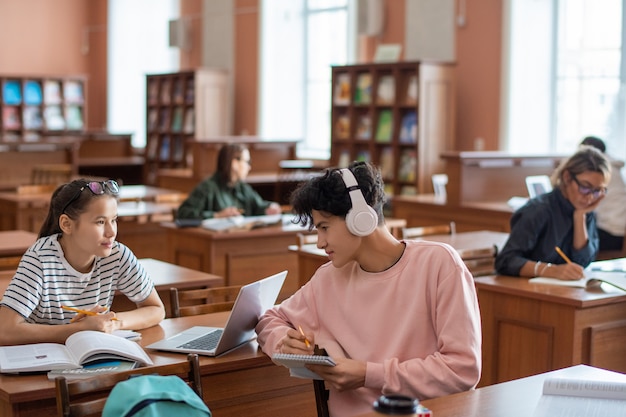 Twee tieners bespreken punten van seminar terwijl ze na de lessen door boeken en online bronnen in de universiteitsbibliotheek kijken