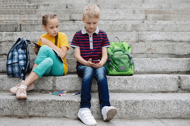 Twee tieners, een jongen en een meisje, zitten op de trap met een smartphone in hun handen.