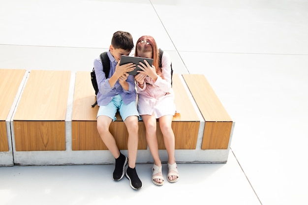 Twee tienerschoolkinderen die tablet spelen terwijl ze op het schoolplein zitten, goed humeur, schooltijd