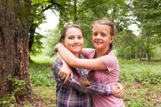 Twee tienerzusjes glimlachen en knuffelen elkaar in het stadspark van de zomer