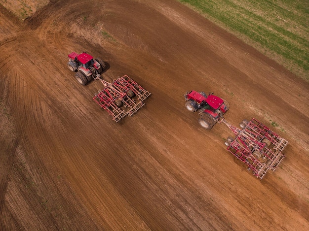 Twee tractoren met een schijveneg ploegen het veld om te zaaien Luchtfotografie